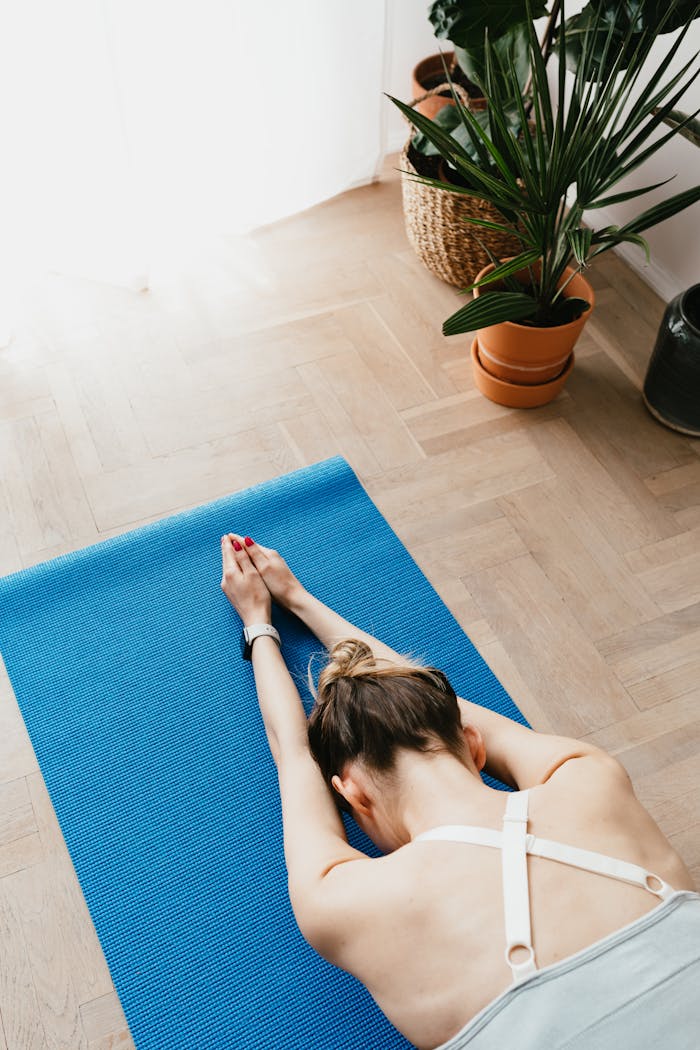 programs-04 Top view of fit faceless lady in sports clothes lying on blue yoga mat in Child pose at home near potted plants